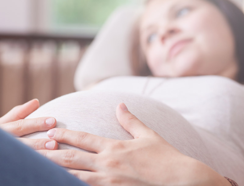 Zwangere vrouw ligt op de sofa en legt de handen rond de buik